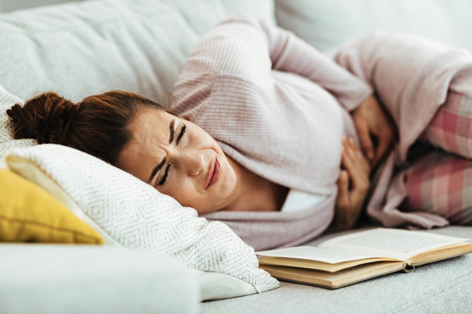 young woman feeling pain her abdomen while lying down sofa home